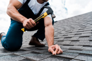 Man holding a hammer while repairing roof shingles